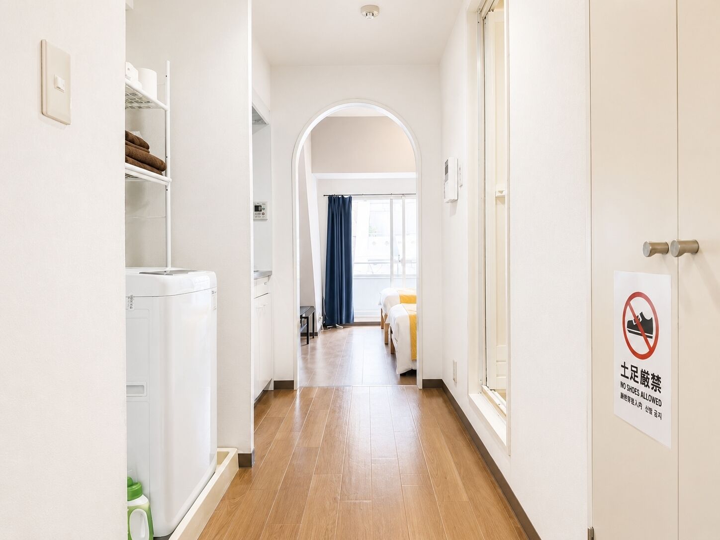 A hotel corridor with a laundry area, a bed, and a sign indicating no shoes allowed.