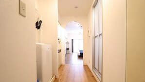 Un couloir étroit au plancher en bois, un réfrigérateur blanc et une porte donnant sur une pièce.