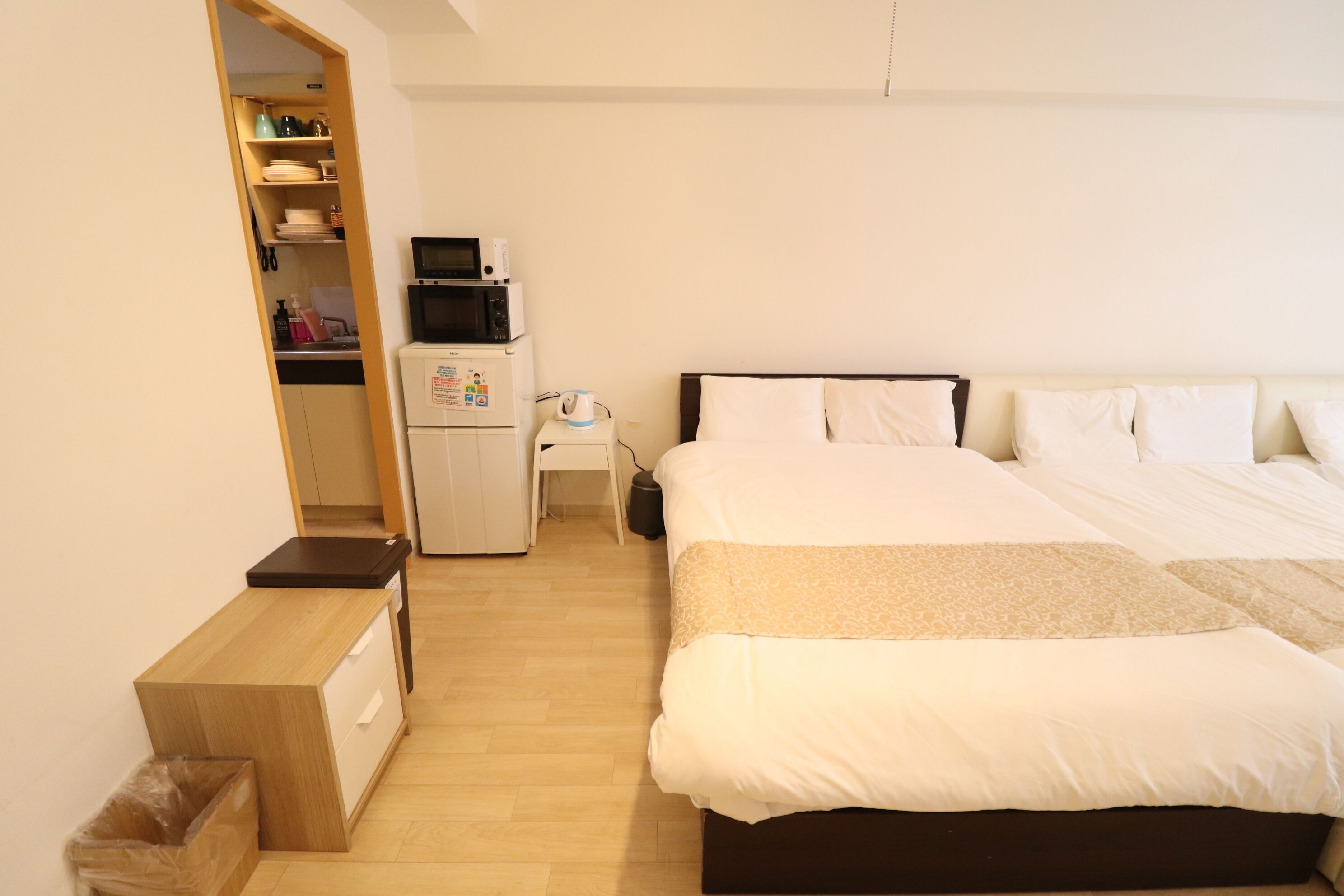 A bedroom with a bed, a desk, a microwave, and a small kitchenette.