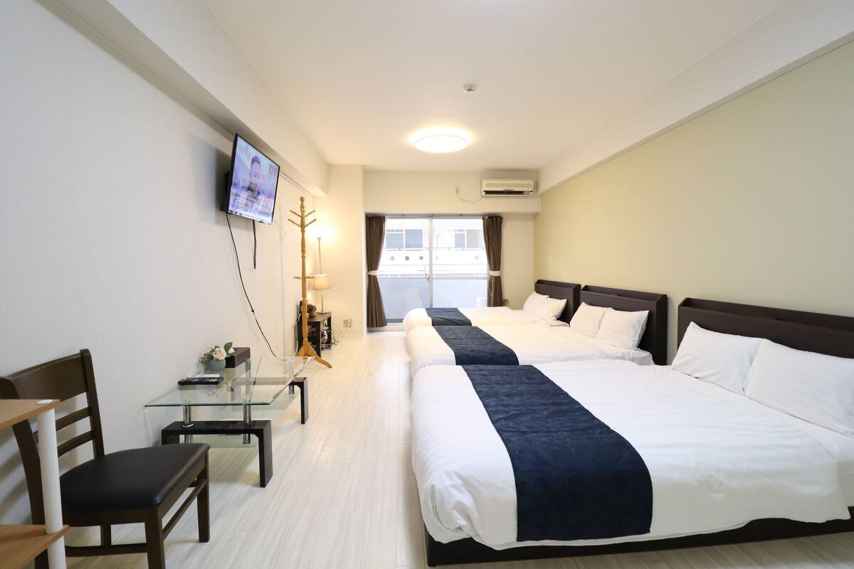 Habitación de hotel con dos camas, un escritorio con silla, un televisor montado en la pared y una ventana con cortinas.