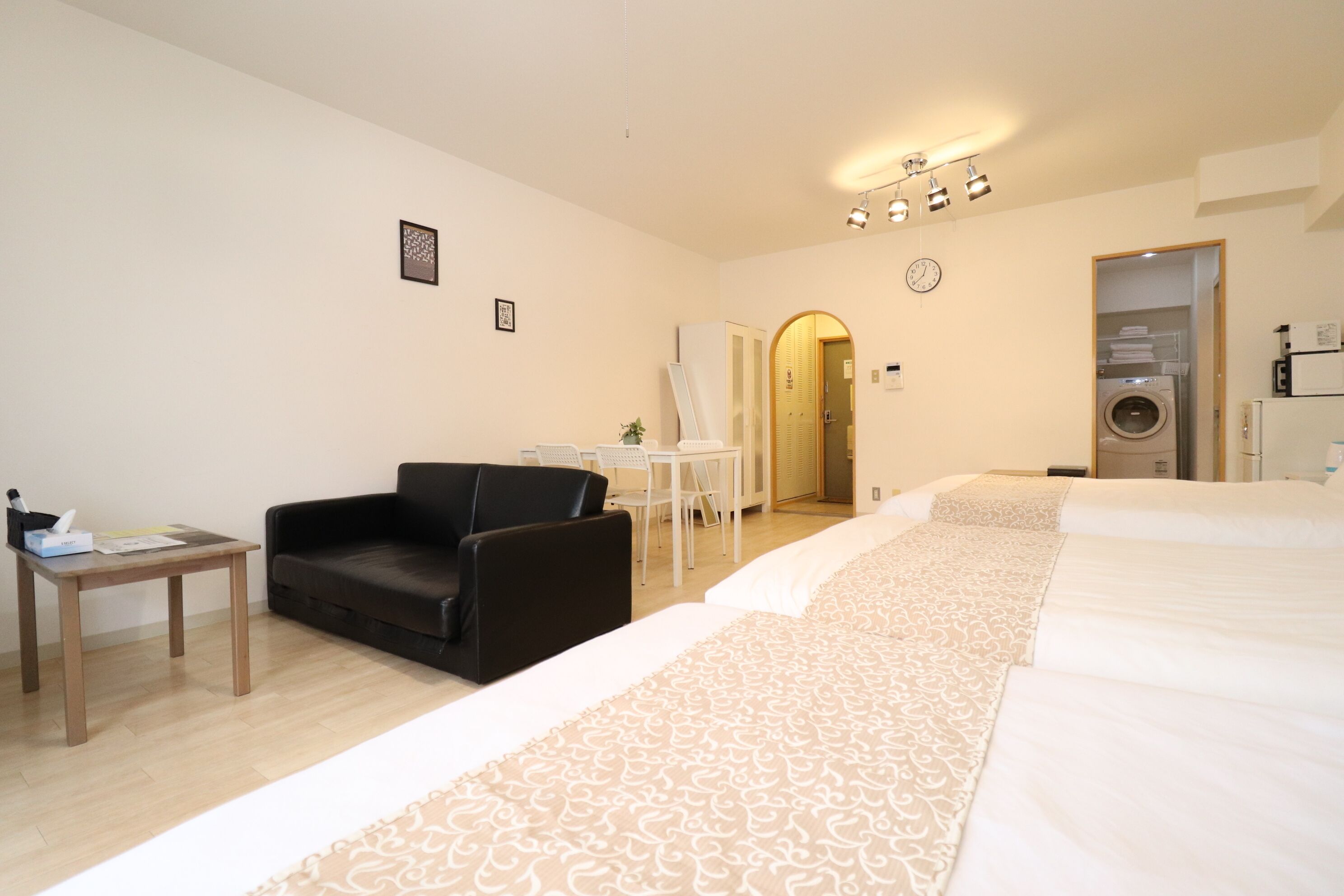 A hotel room with a large bed, a black leather chair, a small table, a washing machine, and a mirror on the wall.