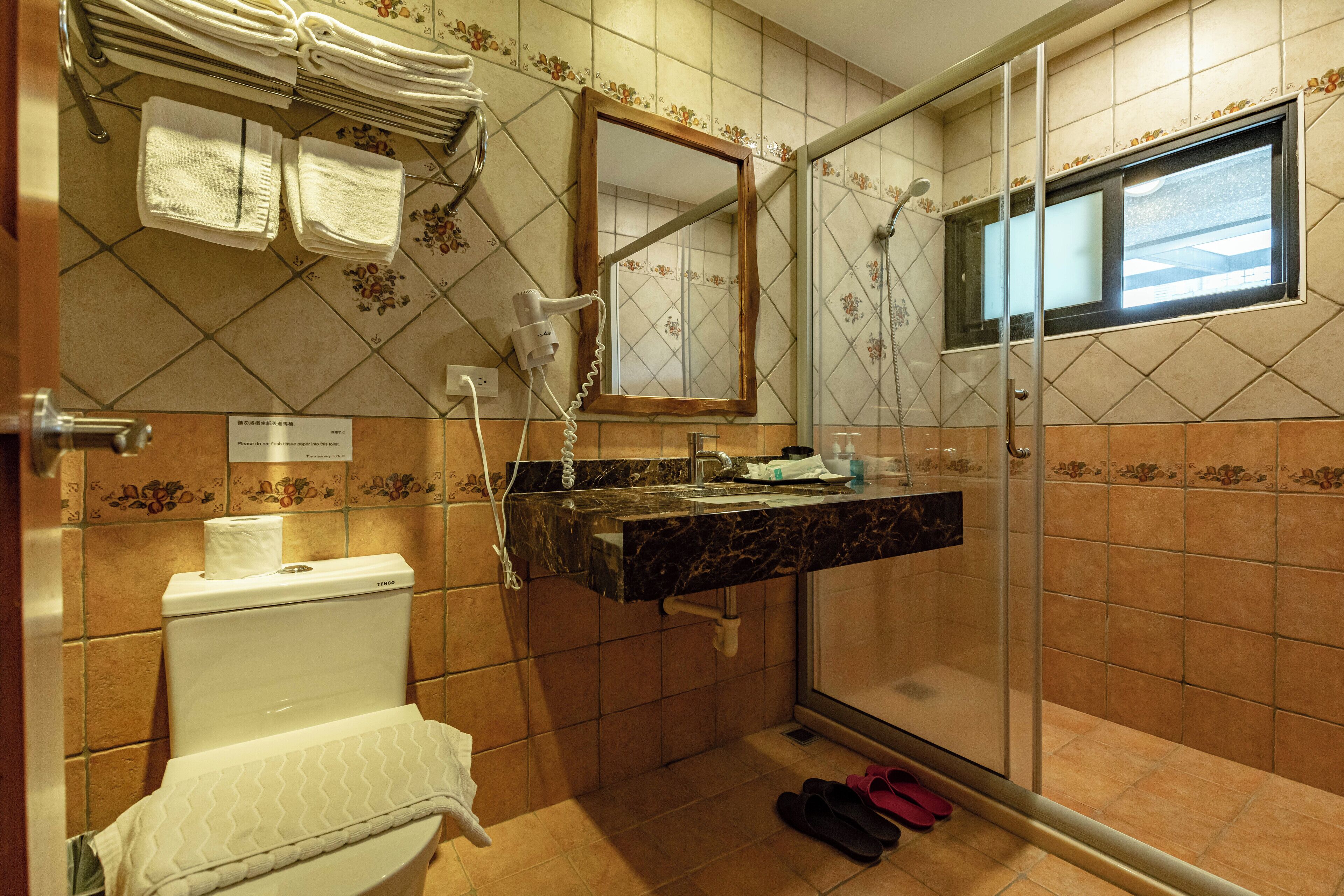 A bathroom with a toilet, sink, and shower. There are towels and a hairdryer on the wall.