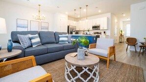 A modern living room with a grey sofa, a coffee table, and a dining area with a wooden table and chairs. - Game Room House - Resort Access (Davenport)