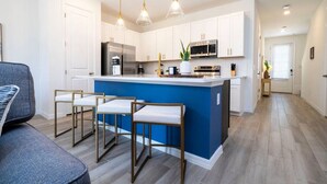 A modern kitchen with white cabinets, a blue island, and a seating area with bar stools. - Game Room House - Resort Access (Davenport)