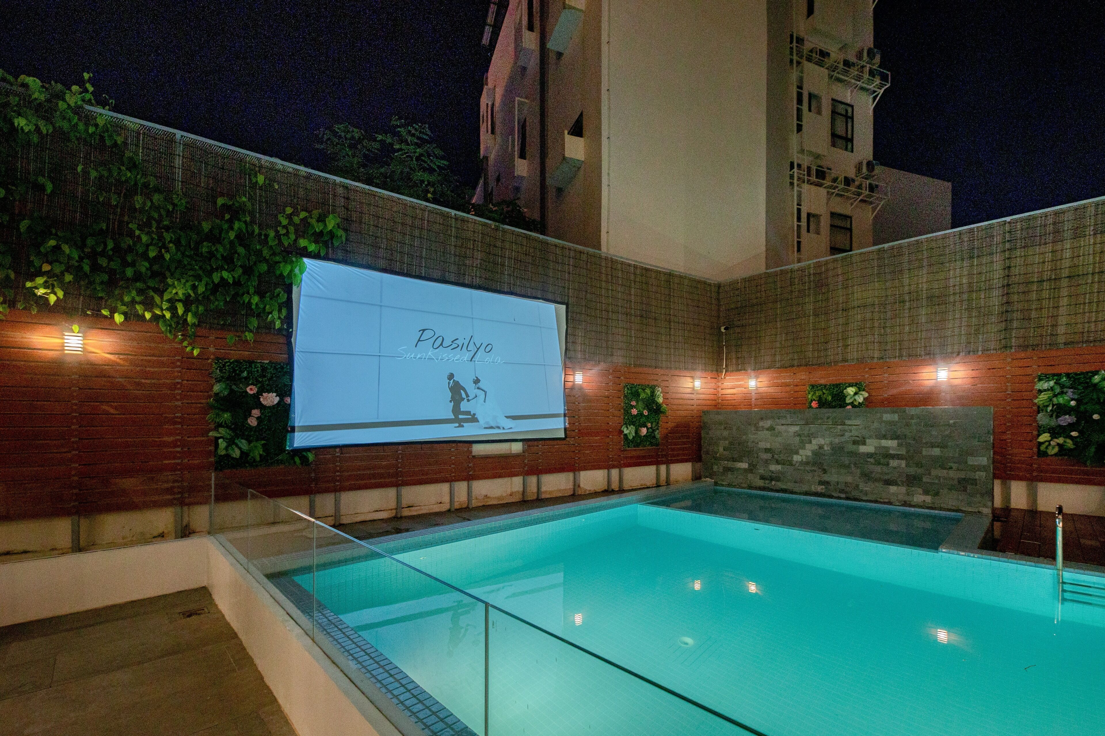An outdoor swimming pool with a glass barrier, surrounded by brick walls and greenery.