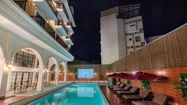 An indoor swimming pool with lounge chairs and umbrellas, surrounded by a brick wall and a balcony with railings. - Solar hotel (Siem Reap)