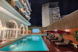 An indoor swimming pool with lounge chairs and umbrellas, surrounded by a brick wall and a balcony with railings. - Solar hotel (Siem Reap)