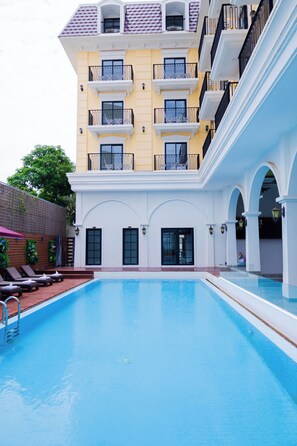 A swimming pool with a clear blue water surface, surrounded by a building with balconies and a white facade.