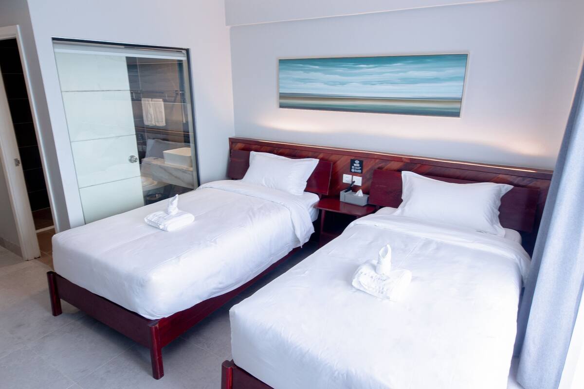 A hotel room with two beds, a wooden headboard, a painting on the wall, and a closet with a sliding door.