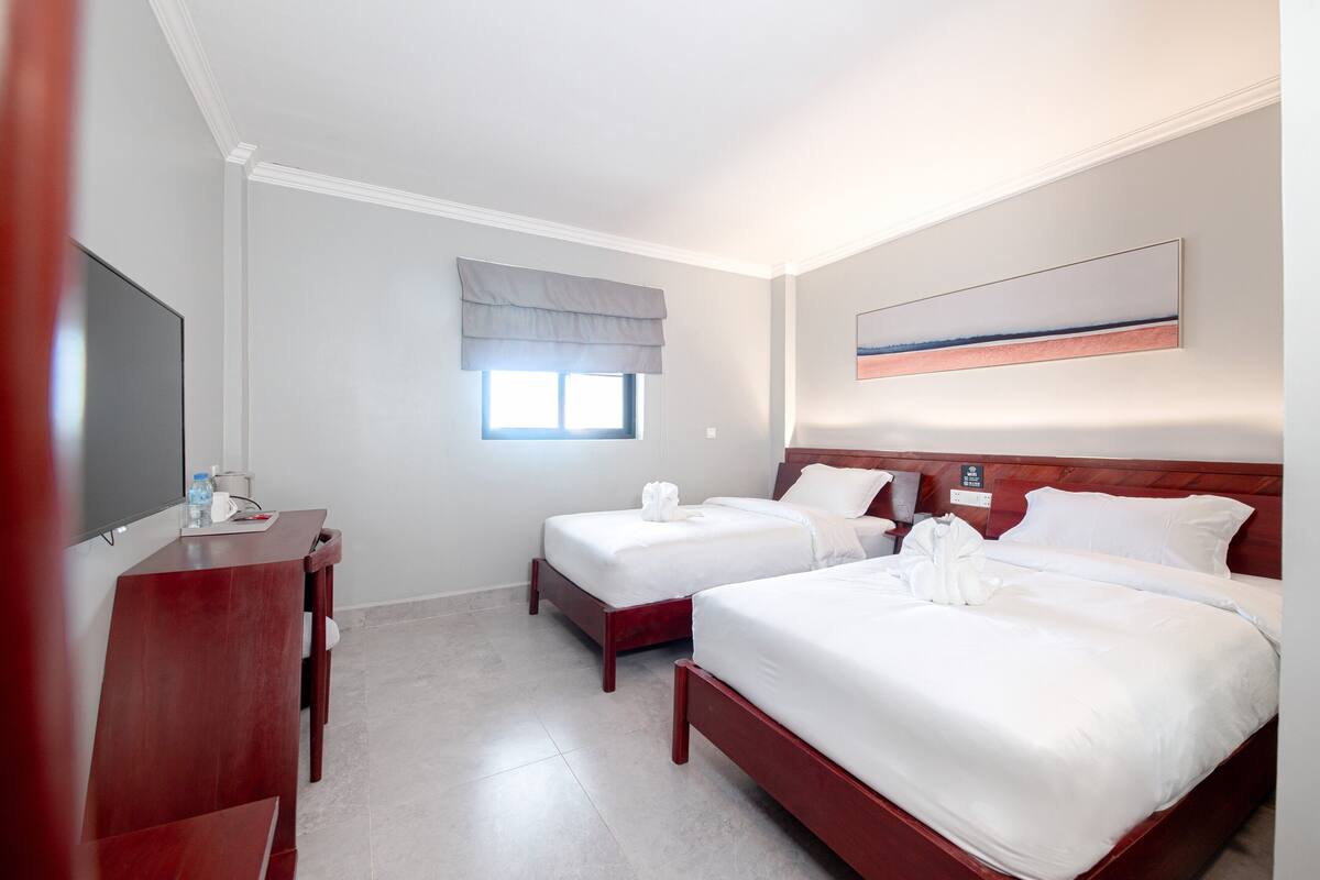 A hotel room with two beds, a desk, a TV, and a window with a view.
