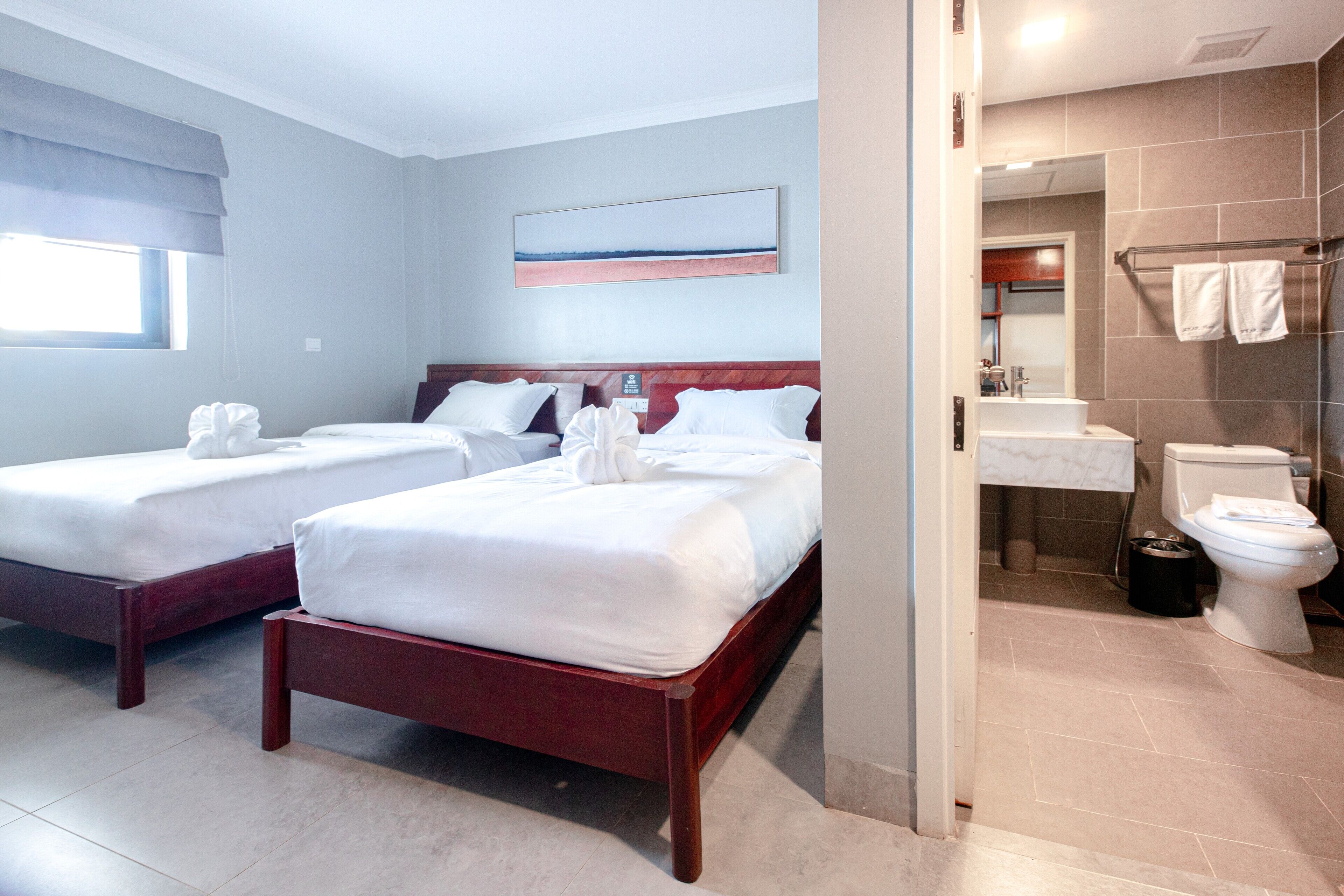 A hotel room with two beds, a bathroom with a shower, and a large window.