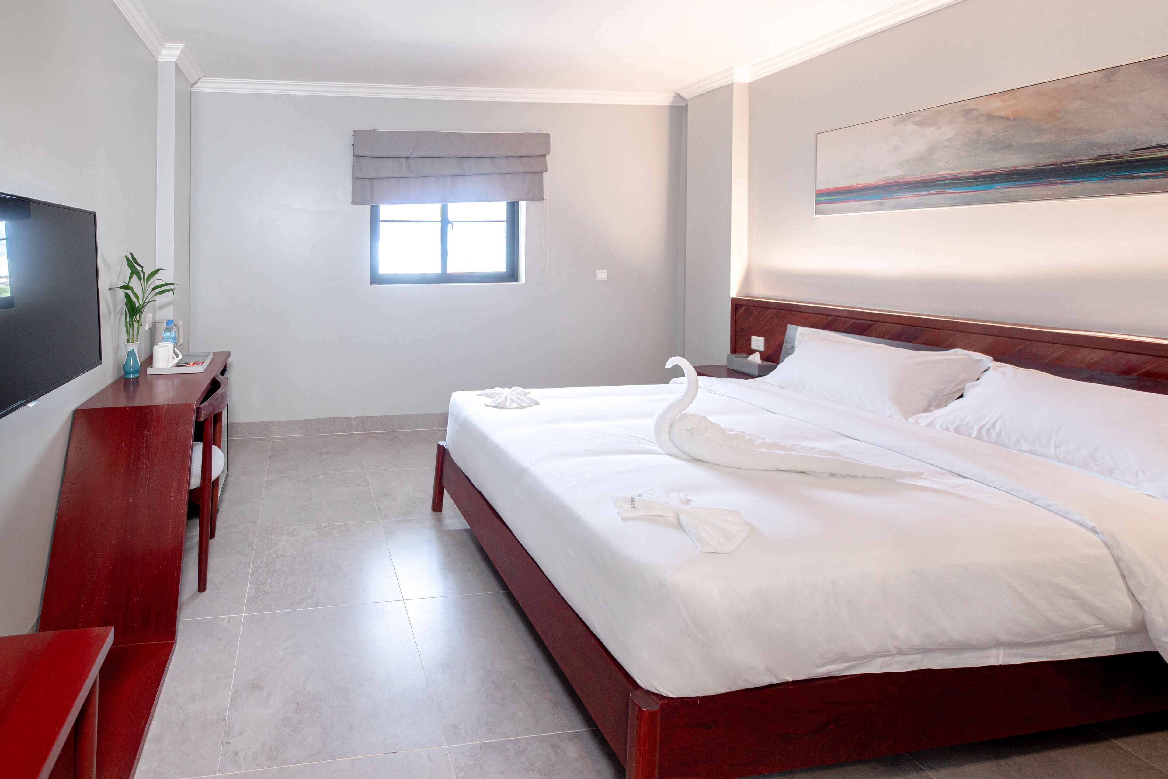 A hotel room with a large bed, a TV, a desk, and a window with a view.