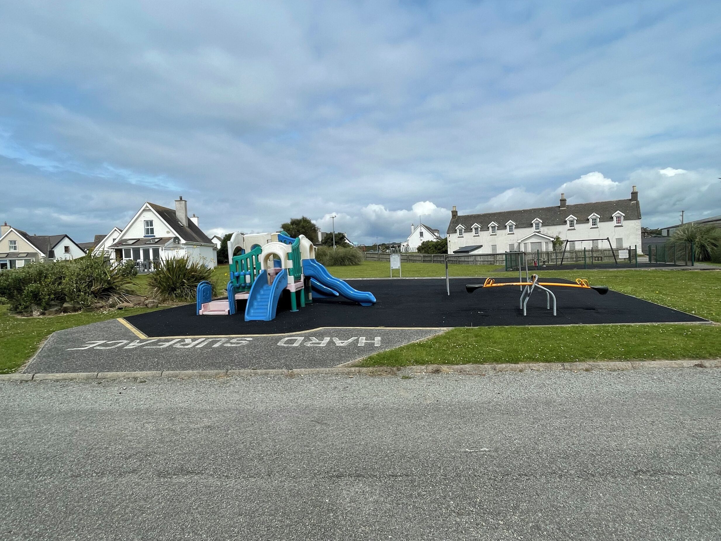 A playground with slides and swings, surrounded by houses and a large building in the background.