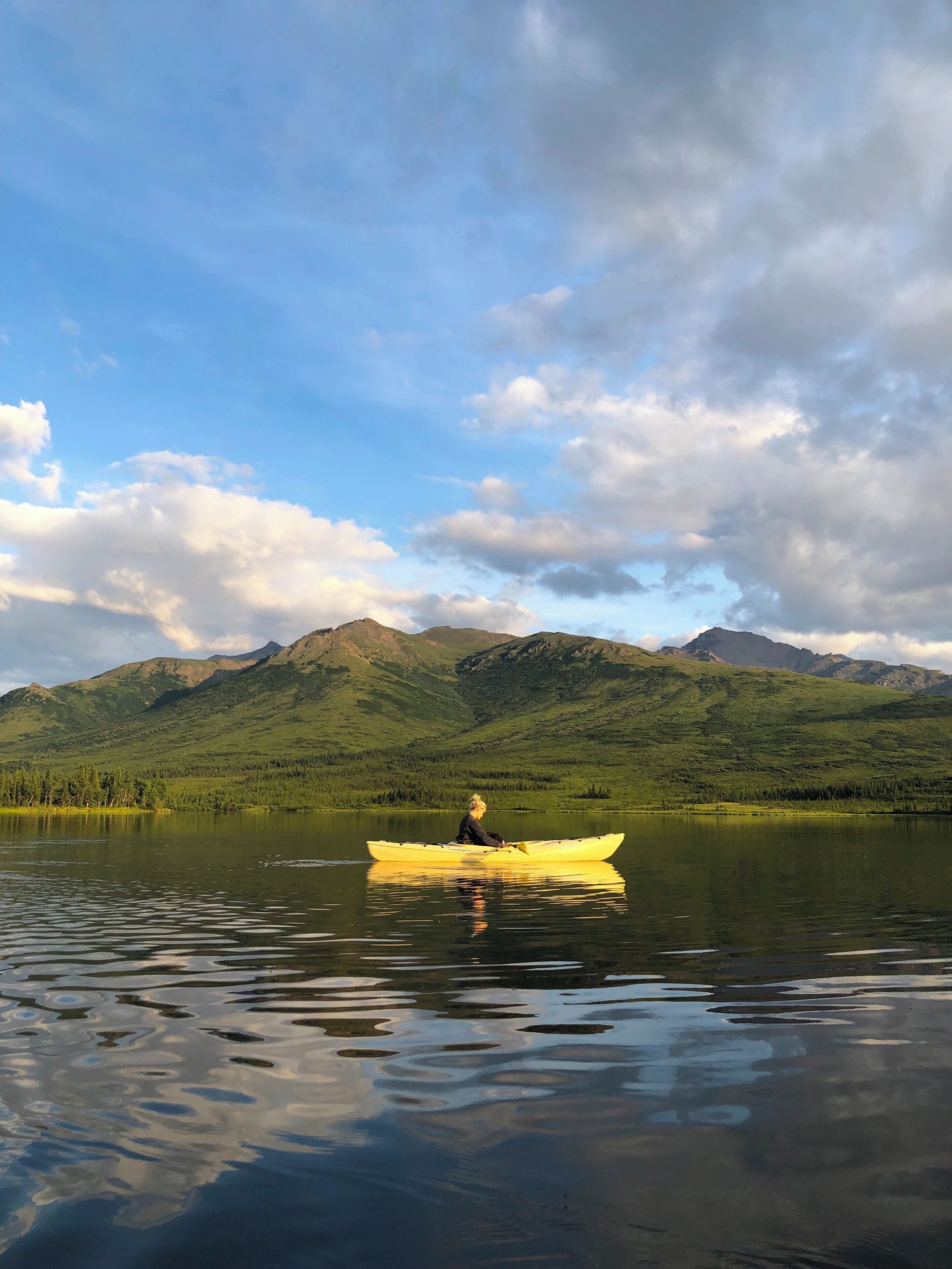 A kayaker in a yellow kayak on a calm lake with mountains in the background.