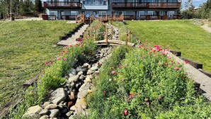 A multi-story building with balconies, a stone pathway, and a grassy area with flowers. - Denali Lakeview Inn (Healy)