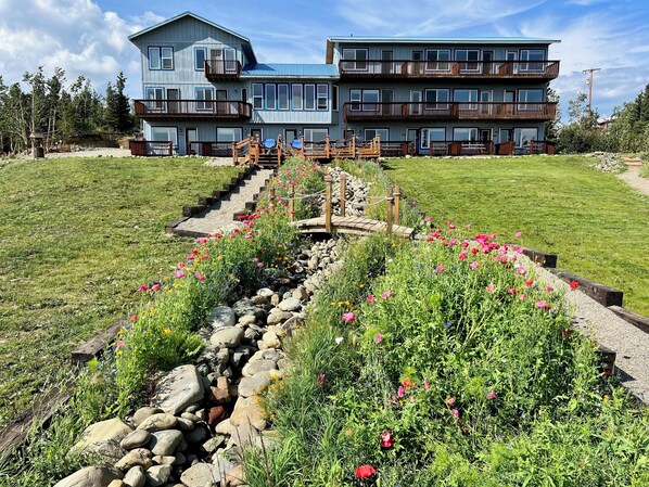 A multi-story building with balconies, a stone pathway, and a grassy area with flowers.