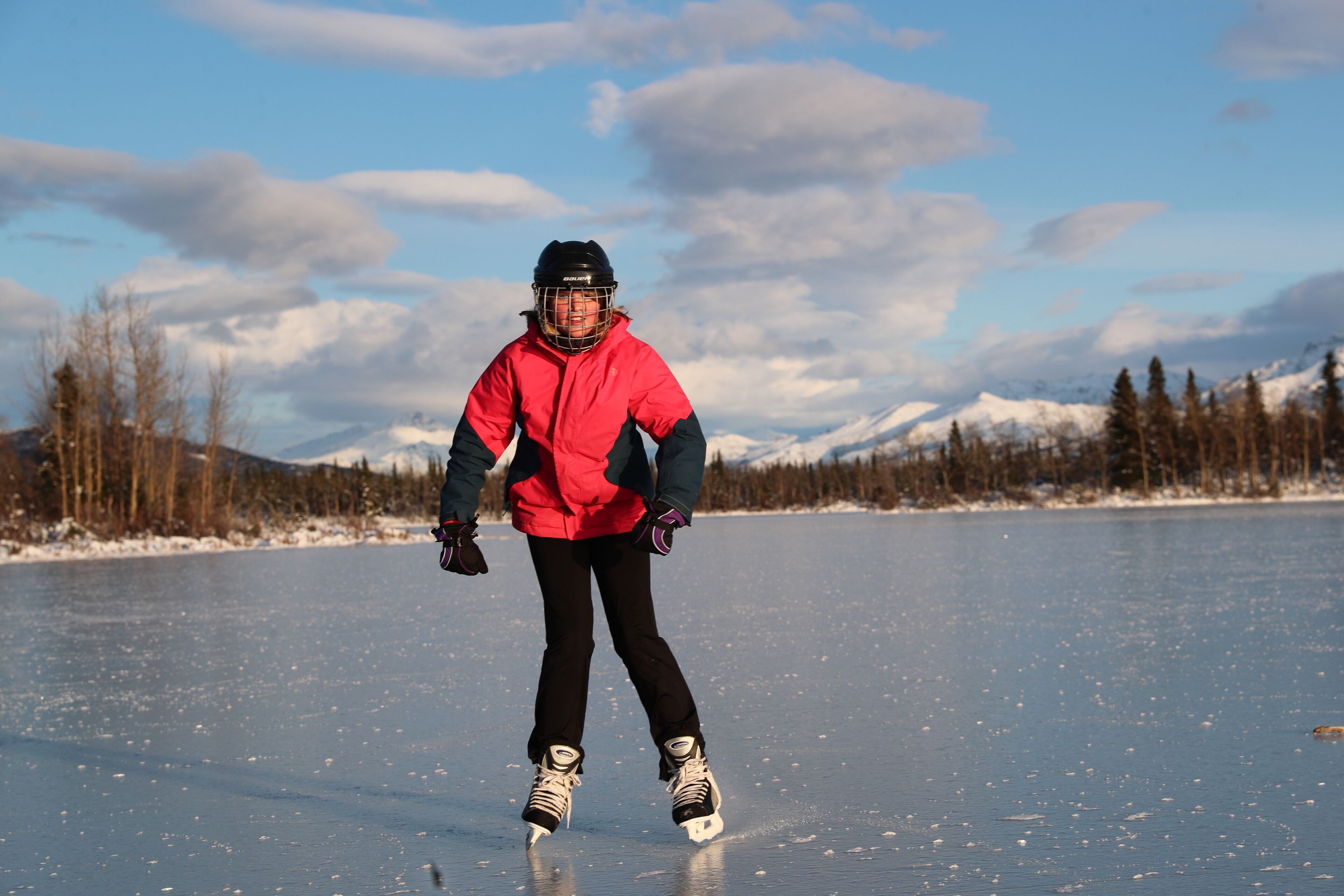 A person ice skating on a frozen lake with mountains in the background.
