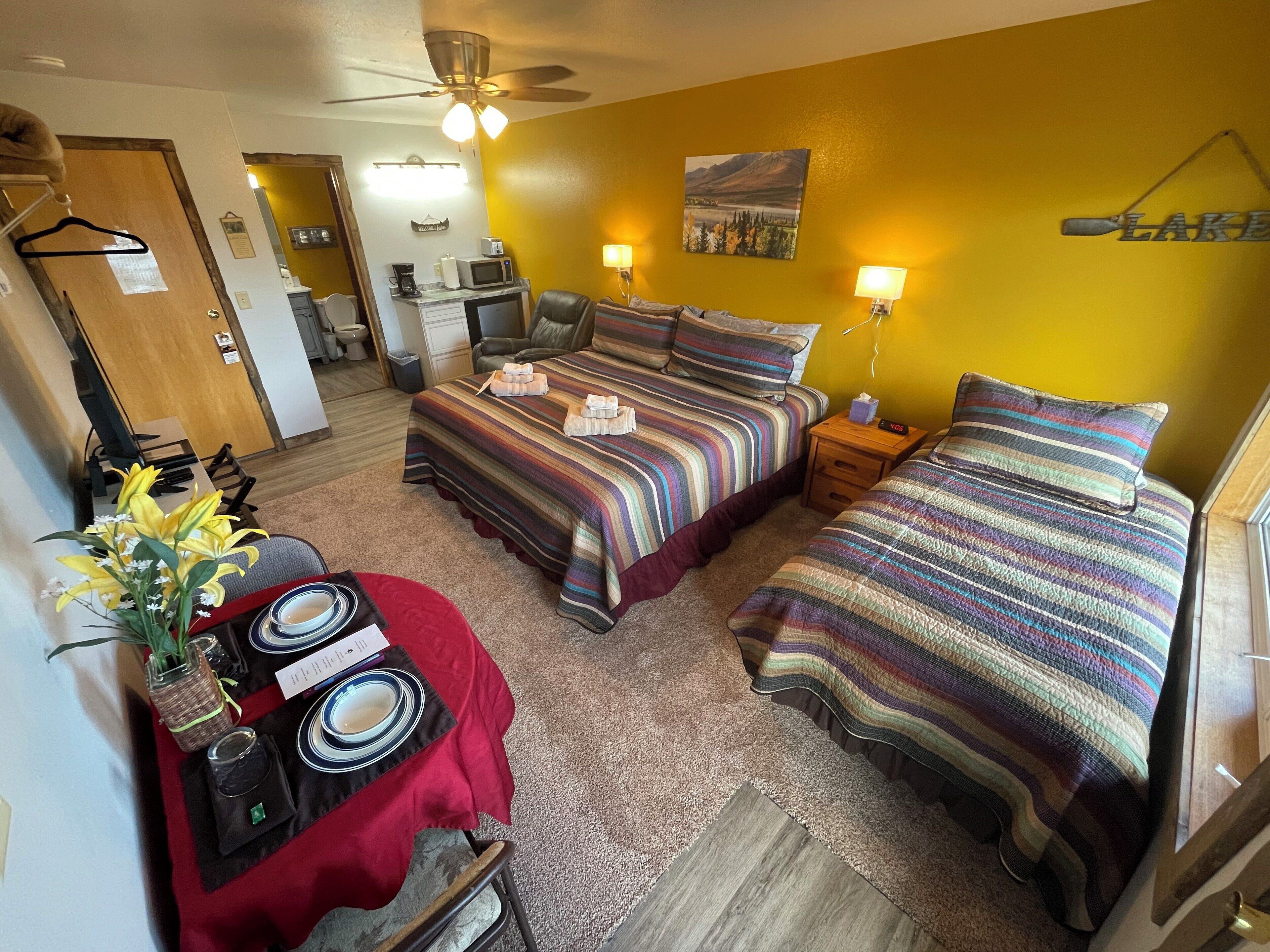 Een hotelkamer met twee bedden, een bureau met een computer, een stoel, een klein tafeltje met een bloevas en een schilderij aan de muur.