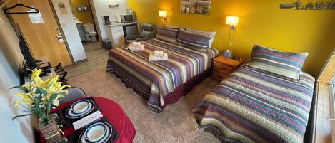 Een hotelkamer met twee bedden, een bureau met een computer, een stoel, een klein tafeltje met een bloevas en een schilderij aan de muur.