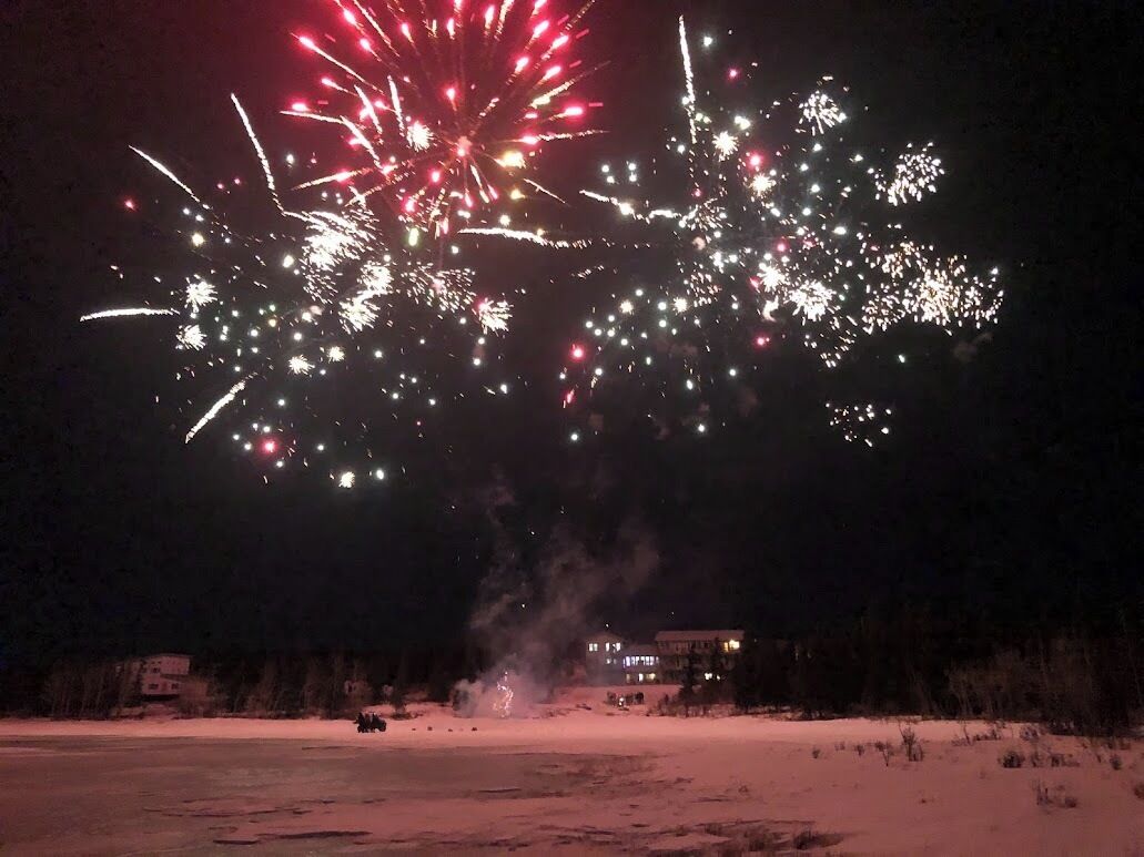 Schneebedeckte Landschaft mit einem Gebäude im Hintergrund und Feuerwerk am Himmel.