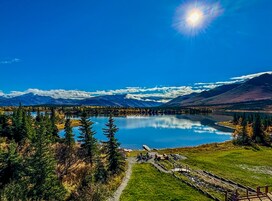 A lake surrounded by mountains, a clear sky, and a wooden deck with chairs.