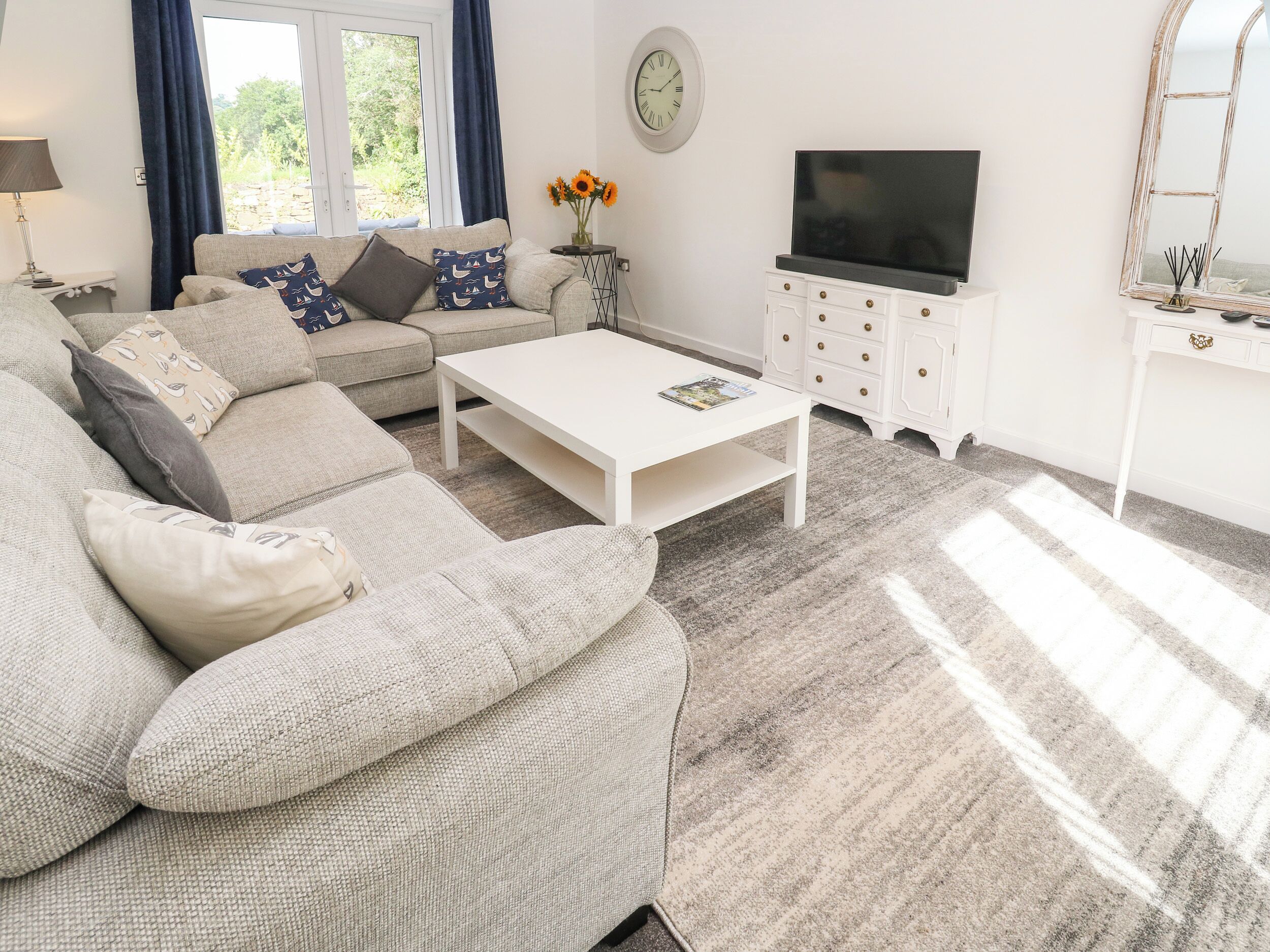 Un salon avec un canapé, une table basse, un meuble pour la télévision et une horloge au mur.