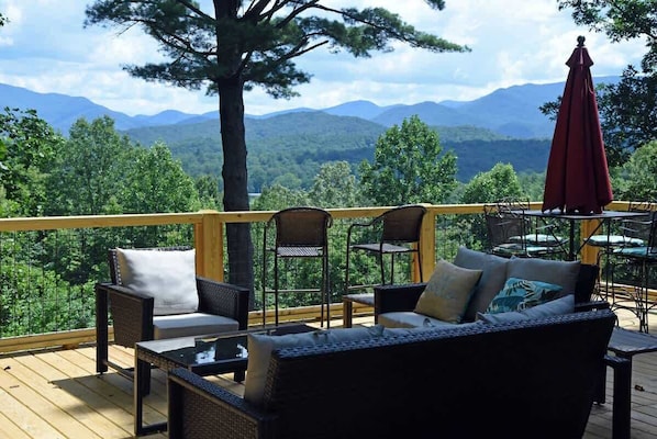 A deck with wicker furniture, a red umbrella, and a view of mountains.