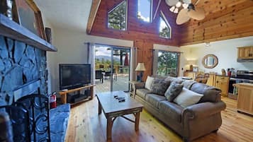 A cozy living room with a stone fireplace, a television, a sofa, and a dining area with a table and chairs.