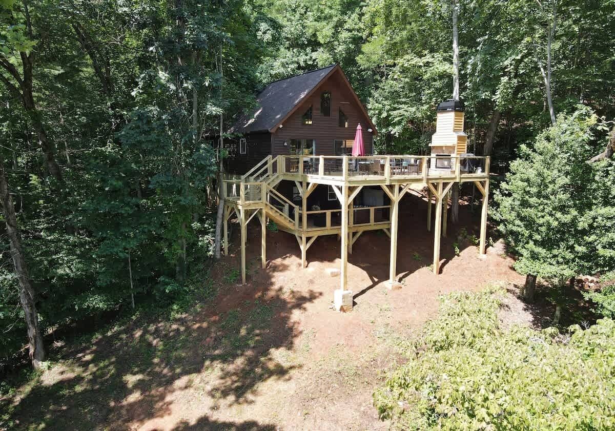 A cabin with a wooden deck, surrounded by dense forest.