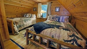 Ein blockhaushaltsähnliches Zimmer mit zwei hölzernen Betten, einem Nachttisch, einem Fenster mit Vorhängen und einer Deckenleuchte.