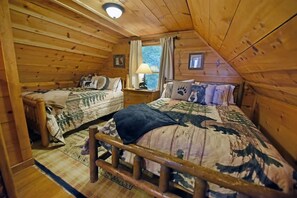 A cabin-style room with two wooden beds, a nightstand, a window with curtains, and a ceiling light.