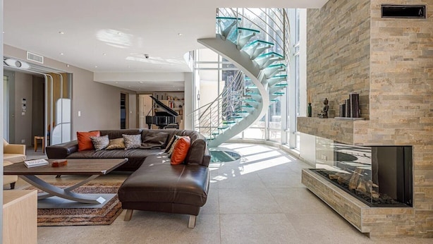 Una sala de estar moderna con una escalera curva, una chimenea y un ventanal grande.