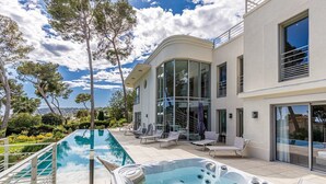 Una casa moderna con piscina, bañera de hidromasaje exterior y sillones de descanso.