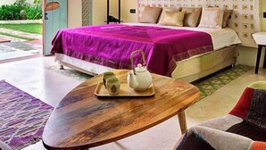 A bedroom with a large bed, a ceiling fan, a painting, and a view of greenery outside. - Parijat Private Pool Villa 1, 2 and 3 BHK (Udaipur)