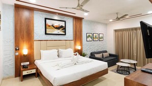 Une chambre d’hôtel moderne avec un grand lit, un canapé, deux petites tables, des ventilateurs de plafond et un téléviseur.