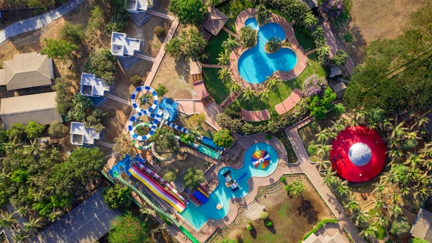 Vue aérienne d’un complexe hôtelier doté de plusieurs piscines, d’un parc aquatique et d’une grande structure en forme de dôme rouge.