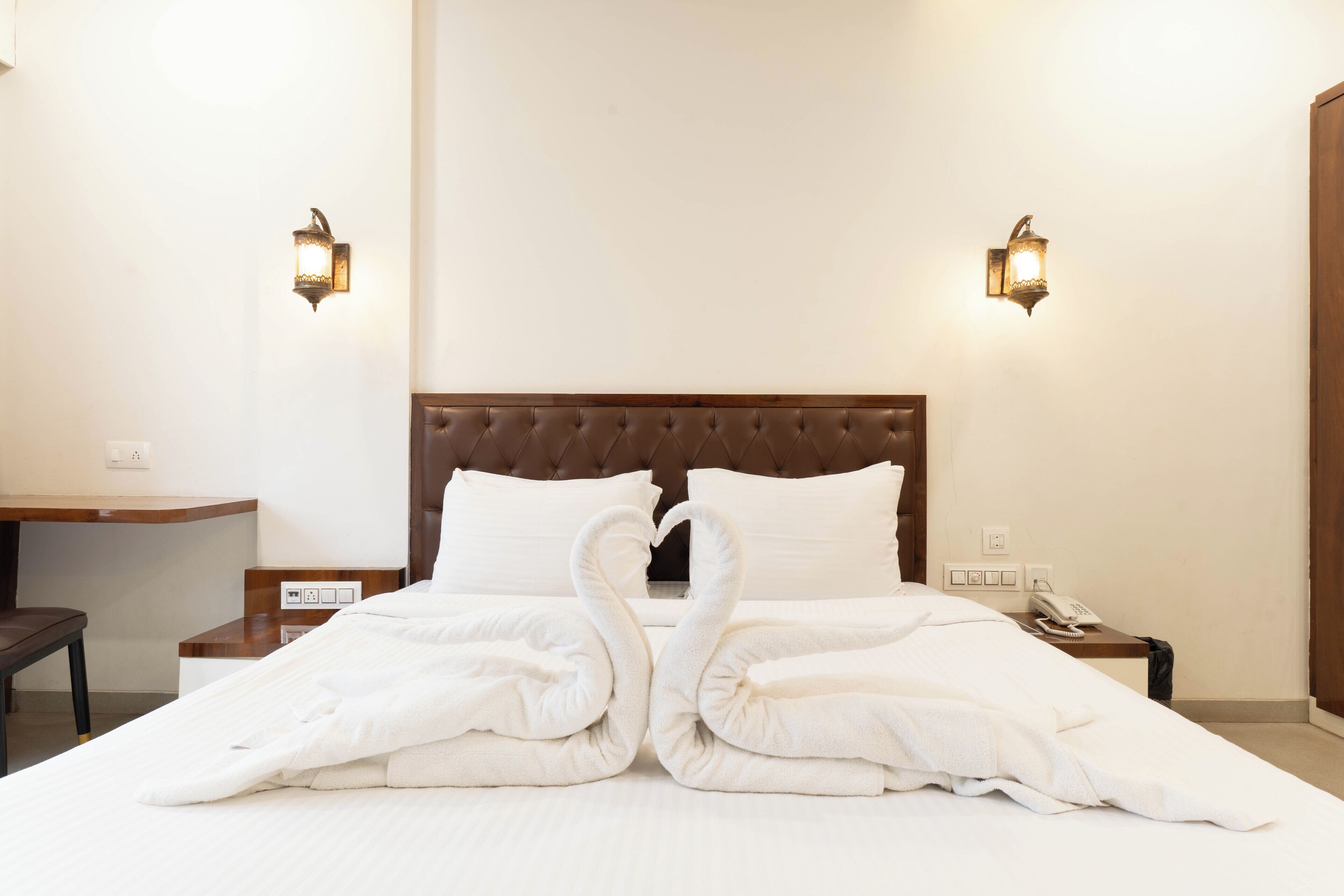 Una habitación de hotel con una cama grande, dos lámparas fijadas a la pared, una mesita de noche de madera, un escritorio y un teléfono.