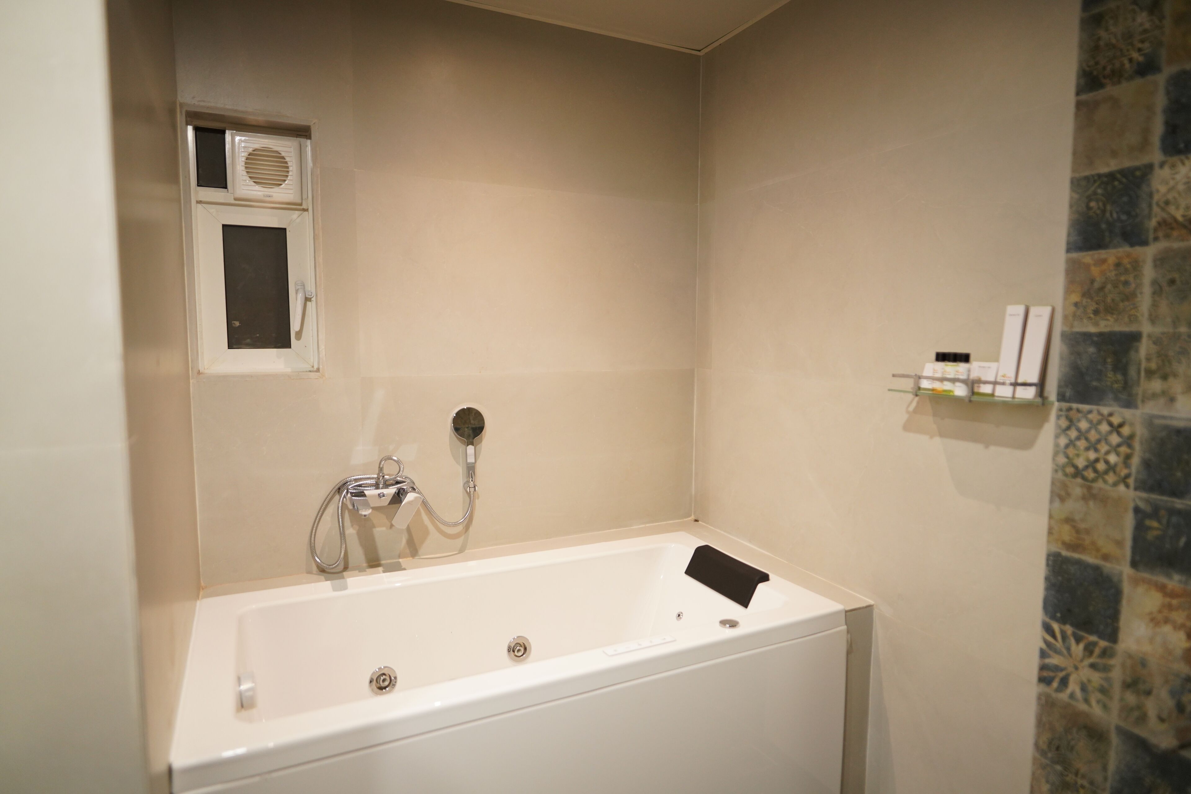 Un baño con una bañera blanca, un cabezal de ducha y un pequeño estante con artículos de aseo.