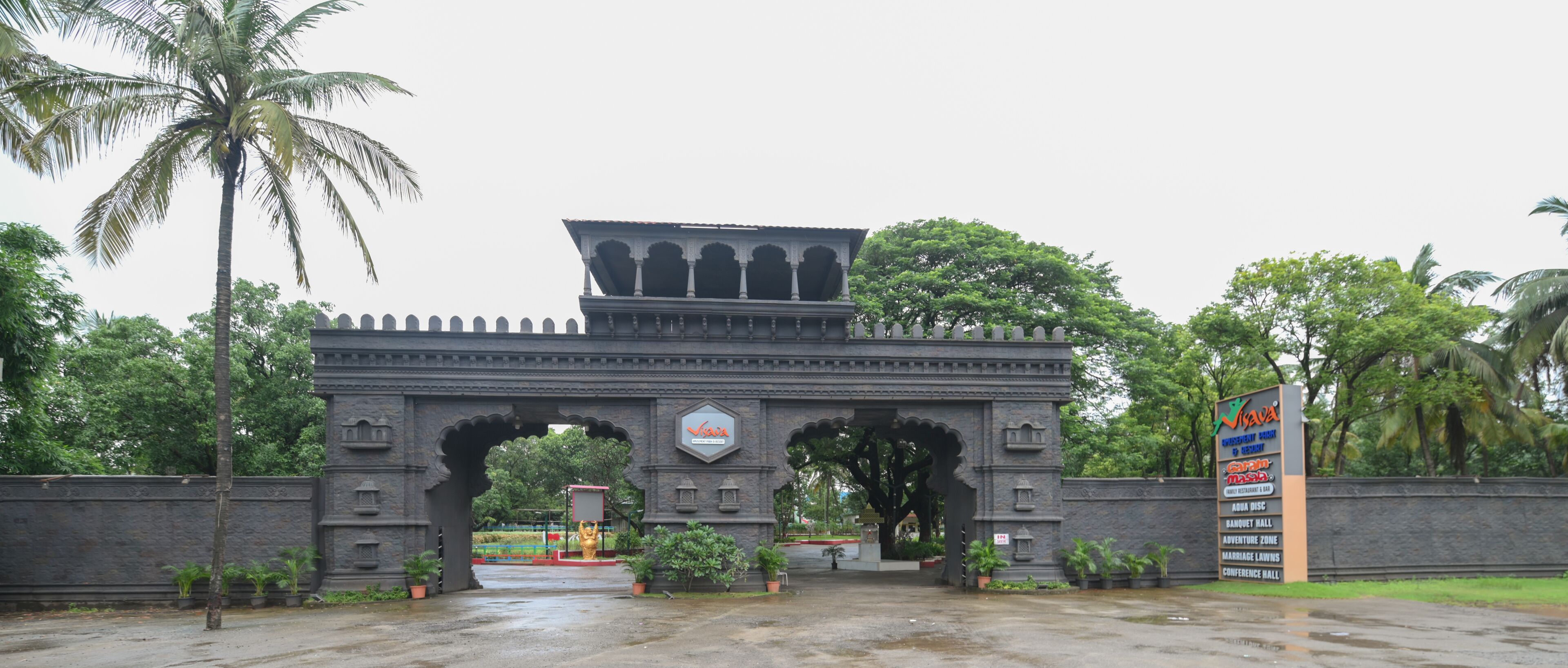 A large stone gateway with arches, surrounded by lush greenery and palm trees.