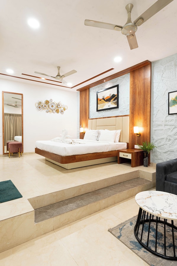 A modern hotel room with a large bed, a seating area, and a ceiling fan.