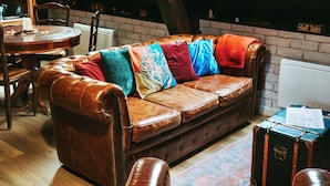 Un espacio tipo loft con un sofá de cuero, una manta escocesa y una mesa de comedor de madera.