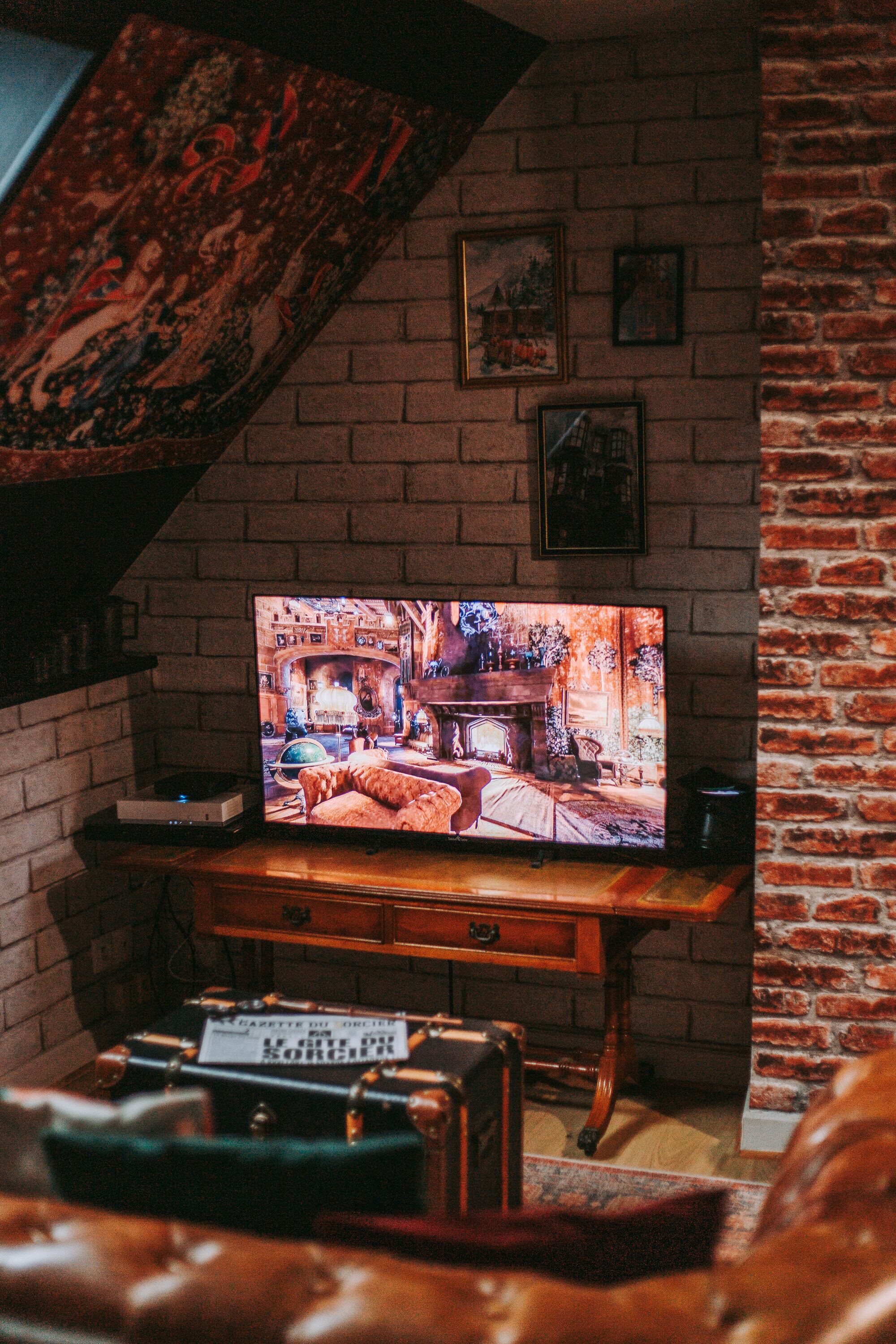 A cozy room with a brick wall, a television on a wooden stand, and a vintage suitcase.