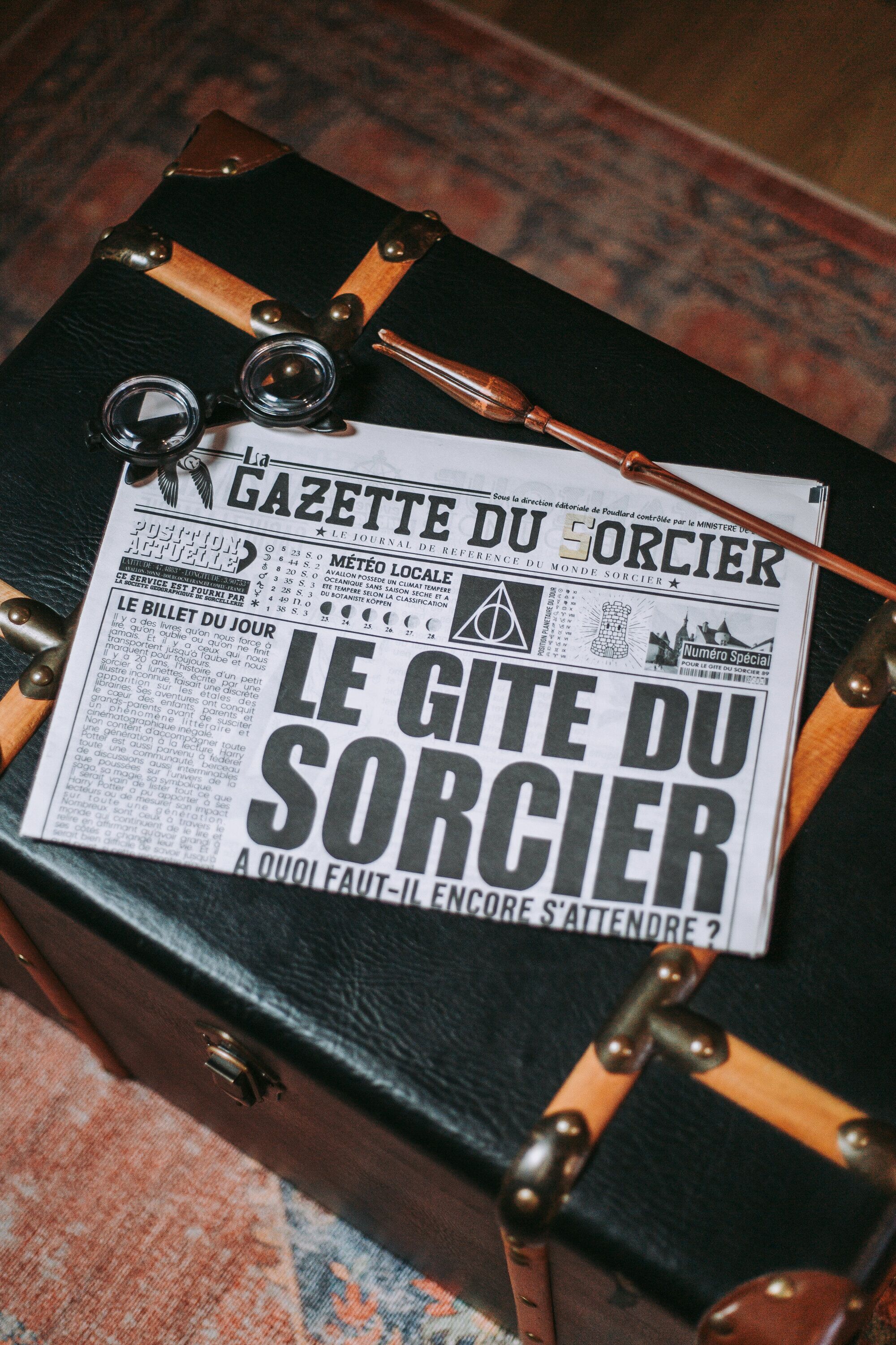 A newspaper titled "Le Gîte du Sorcier" on a black suitcase with metal accents.