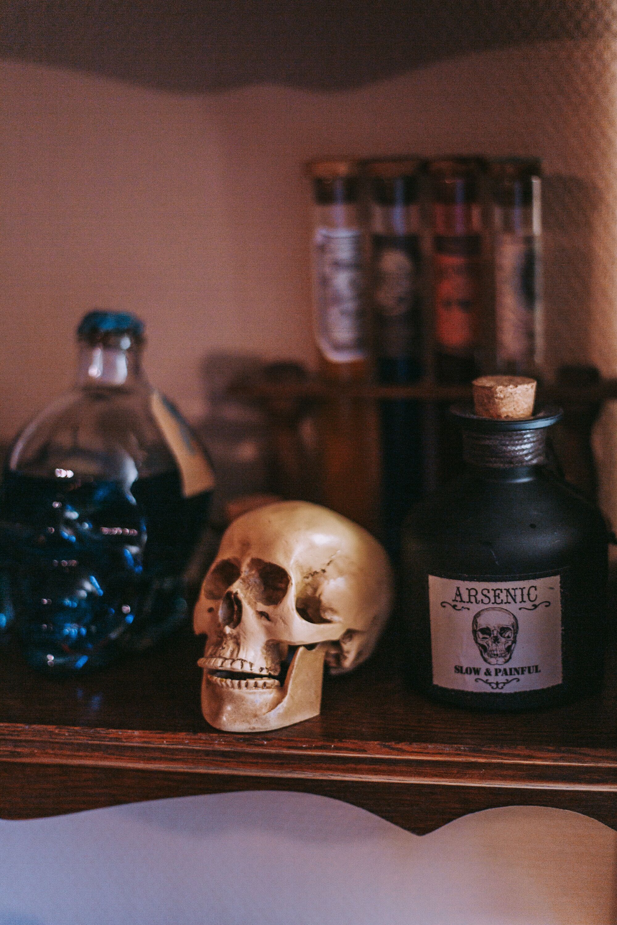 A shelf with a skull, a bottle labeled "ARSENIC," and other bottles in the background.
