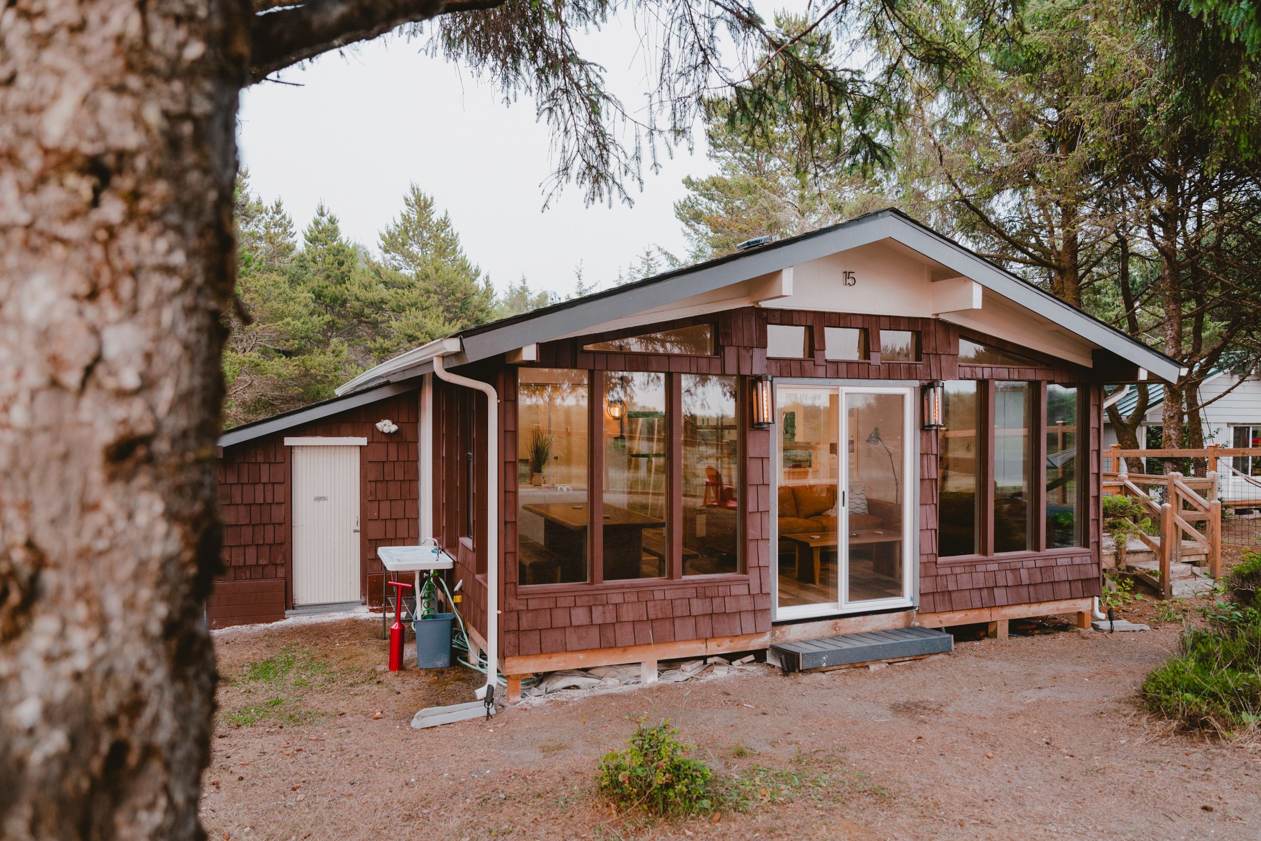 Una petita cabana d'un pis, amb una gran porta de vidre i finestres, envoltada d'arbres.