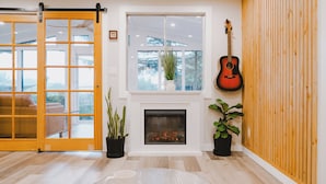 A living room with a fireplace, a guitar, and a sliding glass door leading to an outdoor area. - Remodeled Copalis Beach cottage with fully fenced yard (Ocean Shores)