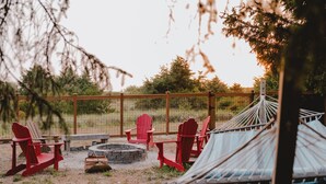 A hammock, a fire pit, and red Adirondack chairs in an outdoor setting. - Remodeled Copalis Beach cottage with fully fenced yard (Ocean Shores)