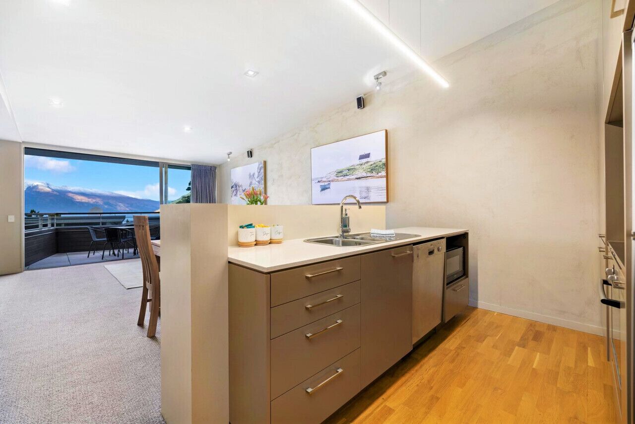 A modern kitchen with a large window, wooden flooring, and a view of the mountains.