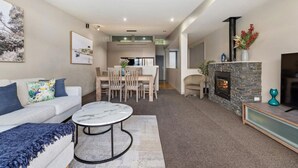A modern living room with a sofa, coffee table, fireplace, and dining area. - Manaaki Alpine Retreat Central CBD ~ SPA ~ Garage (Queenstown)