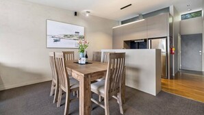 A modern dining area with a wooden table and chairs, a vase with flowers, and a painting on the wall. - Manaaki Alpine Retreat Central CBD ~ SPA ~ Garage (Queenstown)